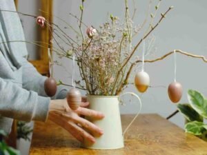 a person holding a vase with flowers and eggs from it